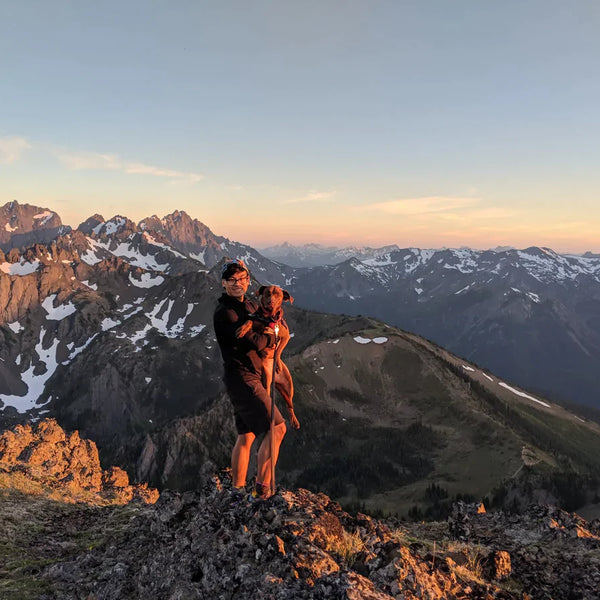 Nathan and Turkey stand on a ridge in the mountains at sunset.